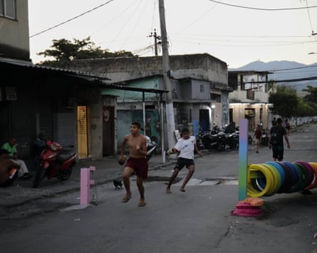 Two boys running on the streets of a favela inbetween colourfully painted barriers. 