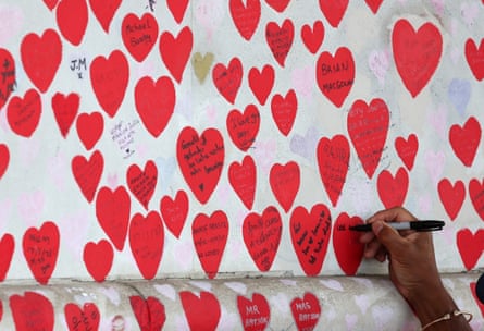 A person writes on a heart on the National Covid Memorial Wall