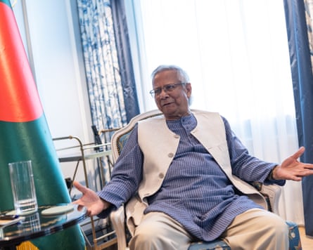 Mohammad Yunus sits in a seat beside a Bangladesh flag