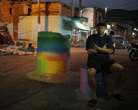 A young man sits on a barricade in the dark. next to a brightly coloured pillar. 
