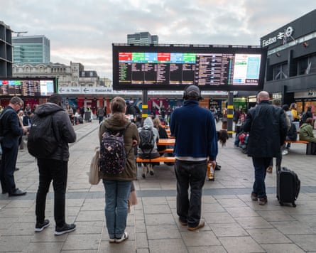People stand with backs to camera looking at information boards outside Euston station