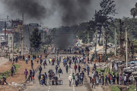 An urban crowd scene of Africans on a main road with black smoke rising in the distance