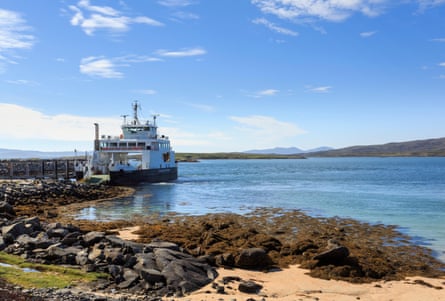 A small ferry by a pier with a sandy beach in the foreground and a blue sky