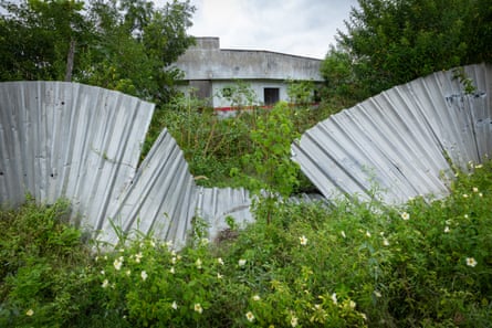 An empty modern building seen through a broken-down metal fence and weeds