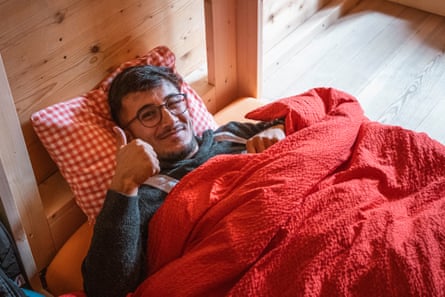 A smiling young man in bed under a red duvet does a thumbs up sign for the camera.