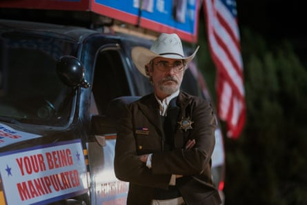 Film still of Joaquin Phoenix standing next to a sheriff’s car.