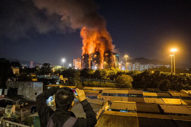 An onlooker takes photos as a major fire engulfs several apartment blocks 