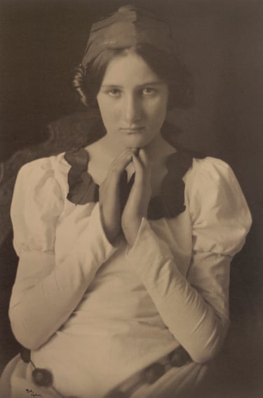 a black and white photo of a woman in a bonnet and white dress with her hands held together under her chin