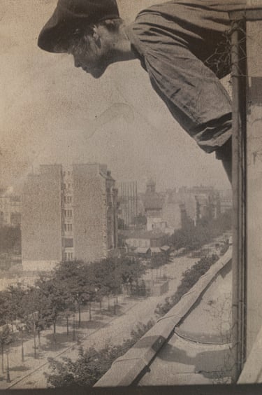 a black and white photo of a woman posing like a gargoyle on the top side of a building, looking down towards the city streets