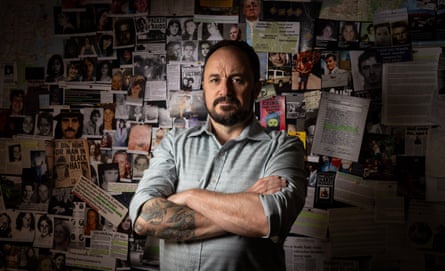 Jeremy Buckingham stands in front of the wall in his office holding images of missing and murdered people in NSW state parliament