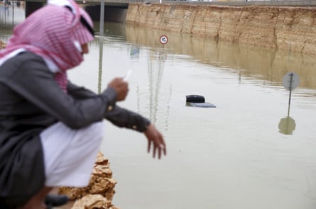 A man on his phone near a car submerged in flood waters following heavy rain in Riyadh