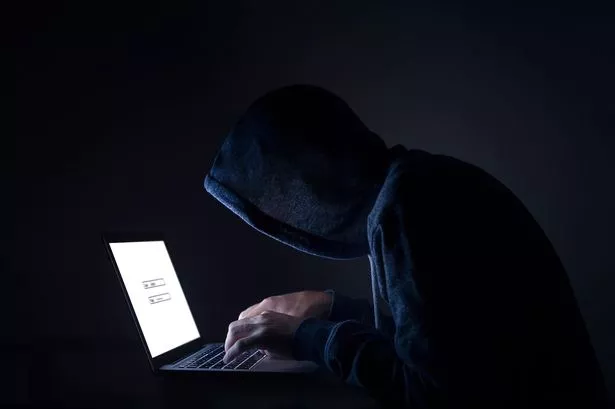 An unidentified hacker in dark hoodie performing at a comupter