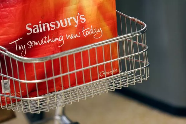A re-useable shopping bag sits in a cart at a checkout desk inside a Sainsbury's supermarket store
