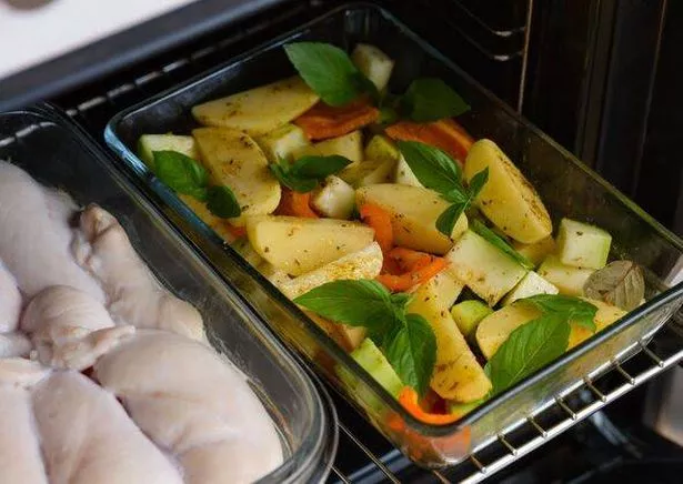 Glass baking trays with chicken breasts and vegetable pieces - potato, zucchini, pepper and basil cooking in the oven.