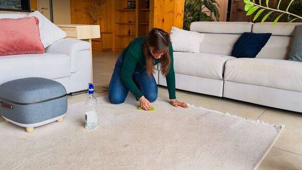 Woman kneels on floor and scrubs a white rug