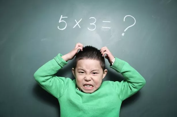 A young Asian boy looking angry in front of a blackboard with a maths equation