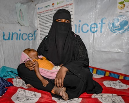 A small and listless baby lies in the lap of a woman wearing a burqa.